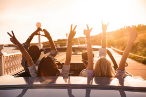 Group of happy young friends in cabriolet with raised hands driv